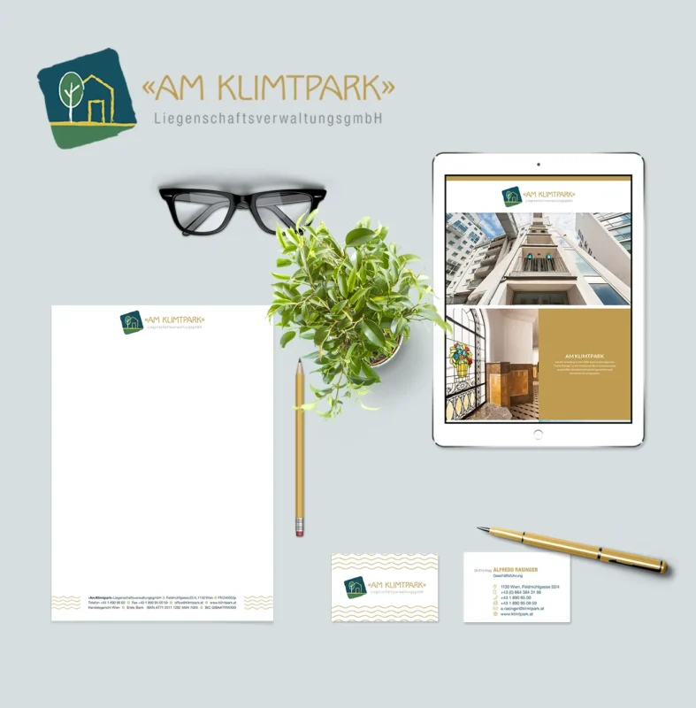 Ein Markenbriefpapierset auf grauem Hintergrund mit dem Logo „AM KLIMTPARK“ zeigt außergewöhnliche Markenidentität. Zu den Artikeln gehören Briefpapier, Visitenkarten, ein iPad mit der Website des Unternehmens, ein Bleistift, eine Brille, ein Radiergummi und eine kleine Topfpflanze. © Pixelflüsterer